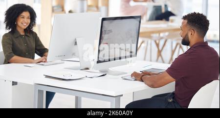 Two happy mixed race businesspeople working on a computer in an office at work. Cheerful hispanic colleagues typing and using a desktop computer while Stock Photo