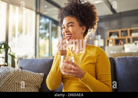 Young happy mixed race woman taking medication with water at home. One hispanic female with a curly afro taking a vitamin for good health while Stock Photo