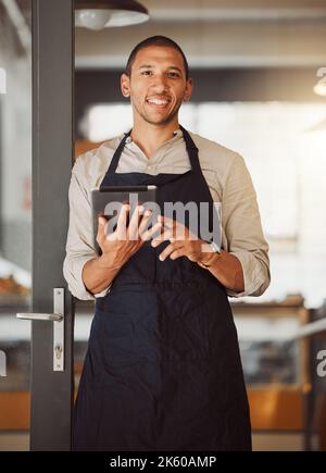 Businessman using a digital tablet in his cafe entrance. Bistro boss using an online app in the restaurant. Young small business owner using a Stock Photo