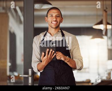 Portrait of businessman using a digital tablet. Mixed race business owner using a wireless digital device. Shop owner standing in entrance using an Stock Photo