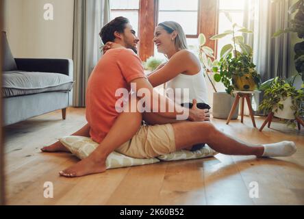 Happy caucasian couple being affectionate and enjoying romantic intimate moment while sitting on living room floor. Young woman sitting on top of Stock Photo
