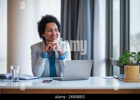 Joyful female african-american company manager in a suit, taking a breather, at the office. Stock Photo