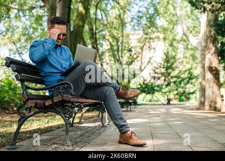 Calm bearded programmer, checking his code on his laptop, in the nature, sitting outside. Stock Photo