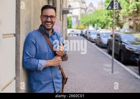 Picture of lovely adult man, tightly holding his tablet, leaning on the wall, preparing to go to work. Stock Photo