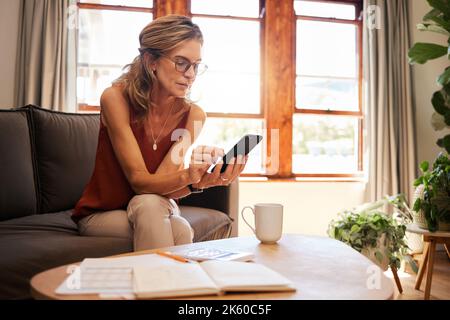 Email, accounting and senior woman planning retirement with help from mobile app and phone on sofa. Elderly accountant reading finance report on the Stock Photo