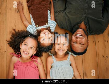 A happy mixed race family of four relaxing and lying on the lounge floor together. Loving black single parent bonding with his kids while being Stock Photo