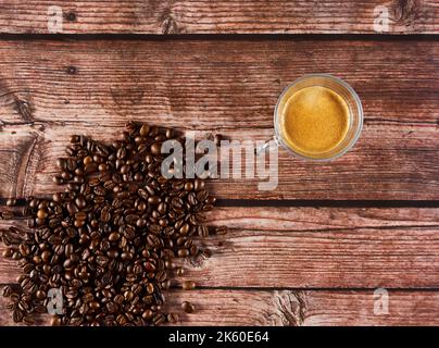 Roasted coffee beans next to cup of coffee on wooden table Stock Photo