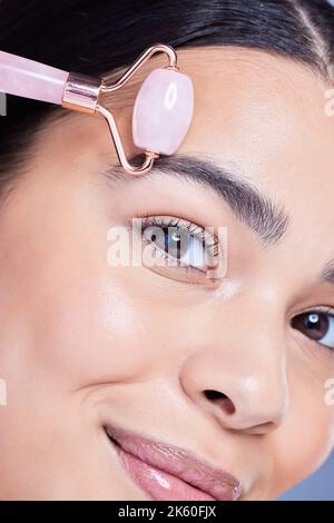 Closeup portrait of a beautiful mixed race woman using a rose quartz derma roller during a selfcare grooming routine. Young hispanic woman using anti Stock Photo