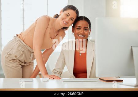 Portrait of two confident young hispanic business women working together on a computer in an office. Happy ambitious colleagues and close friends Stock Photo