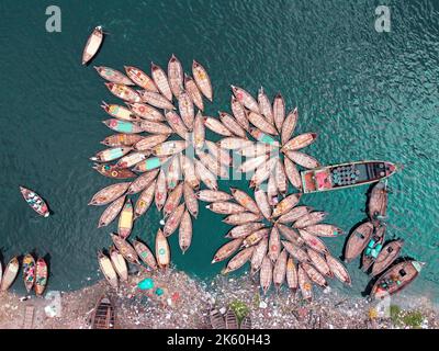 Dhaka, Dhaka, Bangladesh. 11th Oct, 2022. A fleet of wooden boats, which resemble the petals of flower, waits to ferry commuters across the Buriganga River to jobs at a major river port in Dhaka, Bangladesh while boatmen tie the boats together in a flowery pattern and get forty winks ahead of the afternoon rush hour. They work 16 hours a day and get less than Â£5 for this. So, they take rest whenever they get a chance to relieve the fatigue of the long working hours. During that time, most of the boats are tied up together except a few ones and the number of passengers is lower compared to t Stock Photo