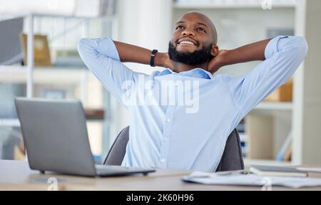Young African american businessman sitting with his hands behind his back while using a laptop in an office alone at work. Content male businessperson Stock Photo