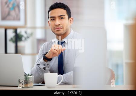 Young serious mixed race businessman working on a laptop alone in an office at work. One focused hispanic businessperson sitting at a desk at work Stock Photo