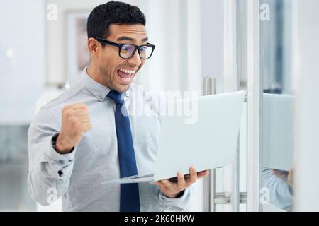 Amazed young mixed race businessman standing and working on a laptop in an office at work. Joyful hispanic male businessperson looking shocked while Stock Photo