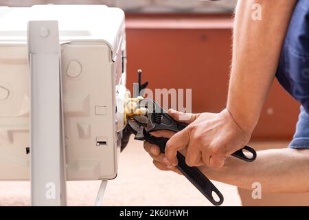 Man holds wrench in his hand. Male technician using spanner when installing modern air conditioning system. Worker on street installs outdoor air cond Stock Photo
