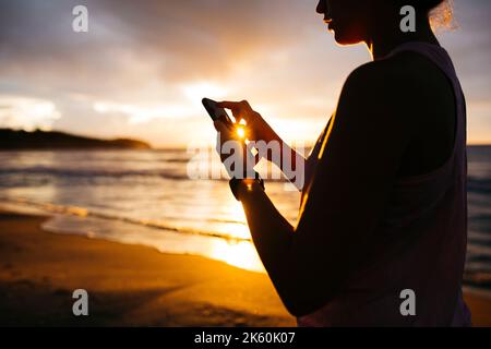 Close up of young woman in sportswear using a phone during working out at the beach at sunset Stock Photo