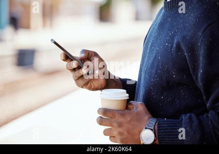 Closeup of Black businessman travelling and waiting for a train while using a cellphone and having a cup of coffee. African american male using a Stock Photo