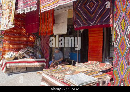 Man weaving handmade carpet in front of his traditional shop, traditional rug sewing man Stock Photo