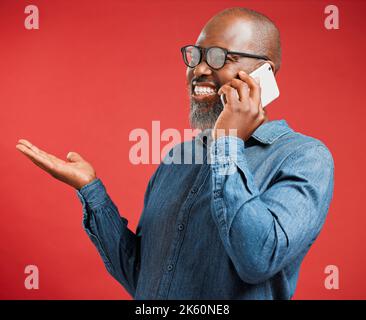 Happy mature African American man isolated against a red background in studio, using hand gestures to ask questions while talking on a cellphone Stock Photo