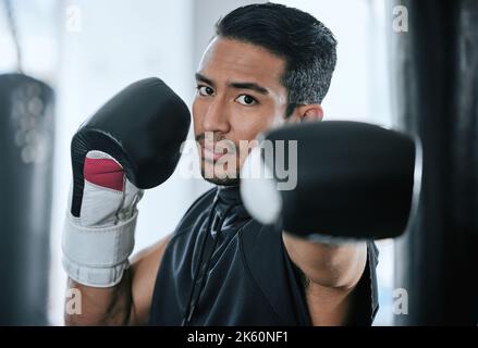 Portrait of serious trainer in boxer stance alone in gym. Asian coach with boxing gloves ready to fight and punch in self defence during health club Stock Photo