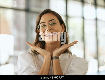 Cheerful business woman with glasses posing with her hands under her face showing her smile in an office. Playful hispanic female entrepreneur looking Stock Photo