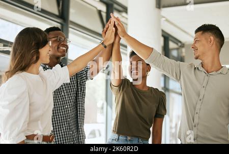 Young colleagues standing in office raising hands to give high five during team building. Diverse business team standing together at startup Stock Photo