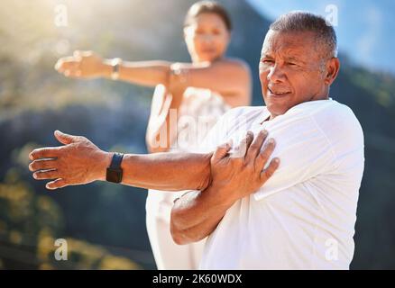 Senior man stretching his arms while exercising outdoors on a sunny day. Mature people practicing yoga together in nature staying healthy and active Stock Photo