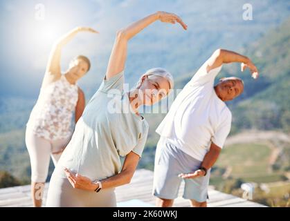 Group of senior people stretching with their hands over heads outdoors. Mature people doing yoga exercise in nature on a sunny day. Yoga class with Stock Photo