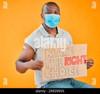 African american covid vaccinated man showing arm plaster, holding poster and wearing surgical face mask. Black model isolated on yellow studio Stock Photo