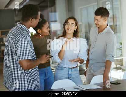 Group of businesspeople standing and talking together in an office. Hispanic businesswoman doing a presentation on a report to her colleagues in a Stock Photo