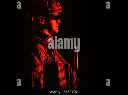 Half length low angle studio shot of special forces soldier in field uniforms with weapons, portrait on black background. Protective goggles glasses are on Stock Photo