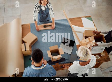 Four diverse clothing designers packing their products working together at a table at work. Tailors making packages while working together from above Stock Photo