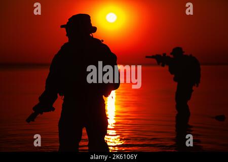 Silhouette of Army soldiers crossing a river against an orange