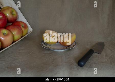 a crate of apples on the left, an apple cut in half in the center, a knife on the right Stock Photo