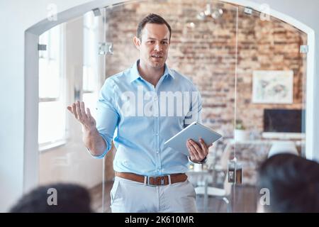 Handsome young architect man using a digital tablet while addressing his colleagues and coworkers during a meeting in the boardroom. Discussing and Stock Photo