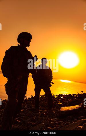 Army soldiers with rifles orange sunset silhouette in action during raid on the river coast Stock Photo