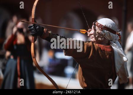 Medieval archery tournament. A woman shoots an arrow in the medieval castle yard. Woman in medieval dress with a wooden bow in her hands. historical Stock Photo