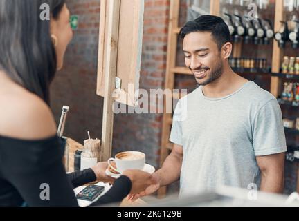Young hispanic waiter serving a cup of coffee to a customer while working in a cafe. Friendly barista and coffeeshop owner managing a successful Stock Photo