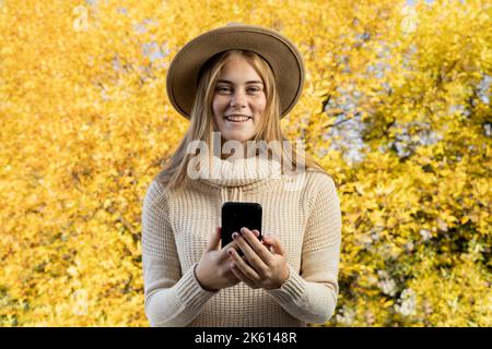 Portrait of happy woman in casual clothes smiles talks walks communicates chat online takes a selfie using a mobile phone technology alone in the Stock Photo