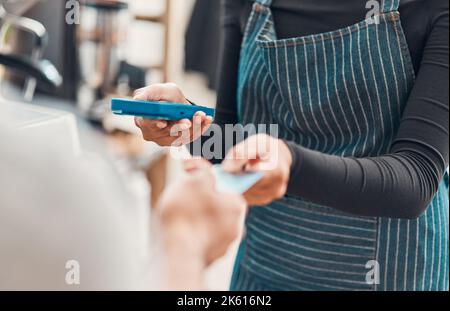 Closeup of a clerk accepting a credit card payment from a customer in a cafe or store. Hands of woman using card machine reader while taking money for Stock Photo