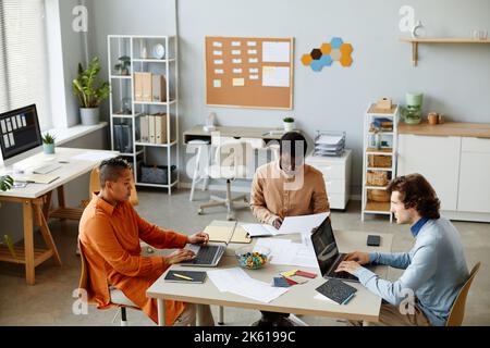 High angle view at diverse creative team of three using laptops while working together at workplace in open office interior, copy space Stock Photo