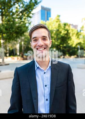 Positive entrepreneur in formal suit smiling and looking at camera while standing on city street in daylight Stock Photo