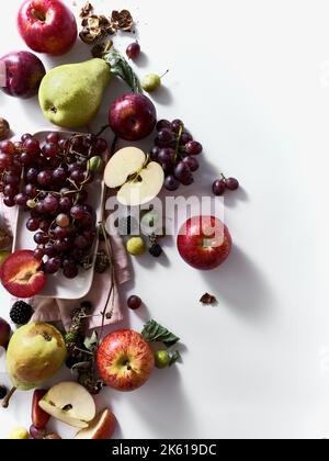 Composition with fresh summer fruits and berries on white background. Grapes, plums and apples in sunlight. Stock Photo