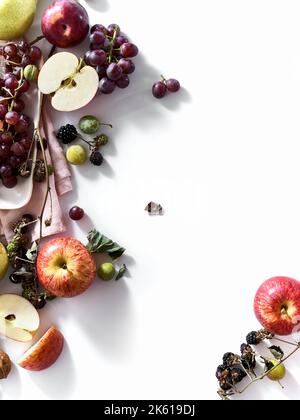 Composition with fresh summer fruits and berries on white background. Grapes, plums and apples in sunlight. Stock Photo