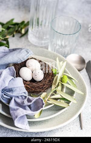 Cutlery set for Easter dinner with olive tree branches and eggs on a bird nest on a concrete background Stock Photo