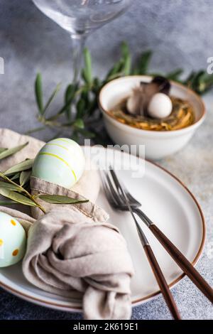 Cutlery set for Easter dinner with olive tree branches and eggs on a bird nest on a concrete background Stock Photo