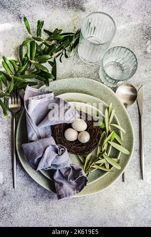 Cutlery set for Easter dinner with olive tree branches and eggs on a bird nest on a concrete background Stock Photo