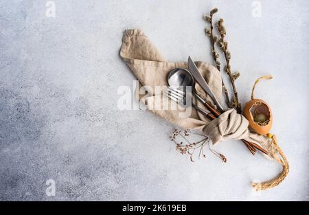 From above cutlery set for Easter dinner with dried flower twig and eggs on a bird nest on a concrete background Stock Photo