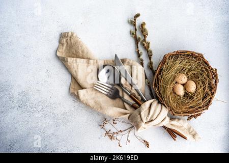 From above cutlery set for Easter dinner with dried flower twig and eggs on a bird nest on a concrete background Stock Photo