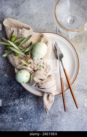 From above cutlery set for Easter dinner with olive tree branches and eggs on plate on a concrete background Stock Photo
