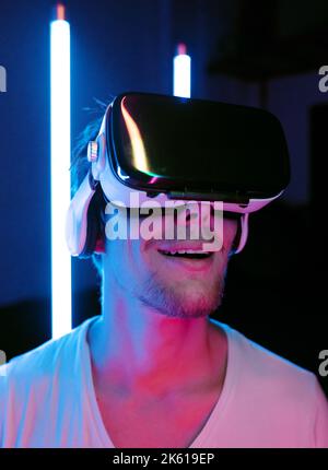 Impressed anonymous unshaven gamer in goggles opening mouth while experiencing virtual reality against neon lights Stock Photo